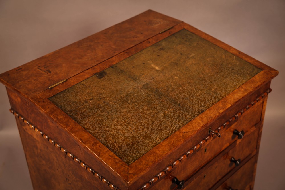 A Victorian burr oak Davenport desk featuring a green leather writing slope, side drawers with wooden knobs, bead moulding, and brass casters. View XV