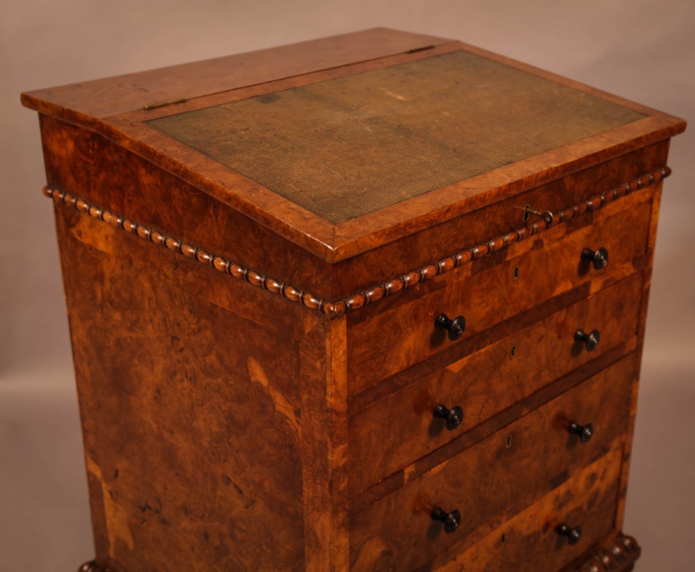 A Victorian burr oak Davenport desk featuring a green leather writing slope, side drawers with wooden knobs, bead moulding, and brass casters. View XVI