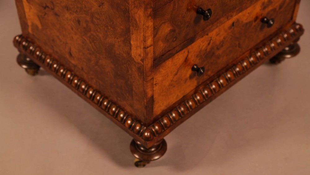 A Victorian burr oak Davenport desk featuring a green leather writing slope, side drawers with wooden knobs, bead moulding, and brass casters. View XVII