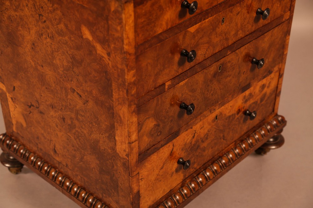 A Victorian burr oak Davenport desk featuring a green leather writing slope, side drawers with wooden knobs, bead moulding, and brass casters. View XVIII
