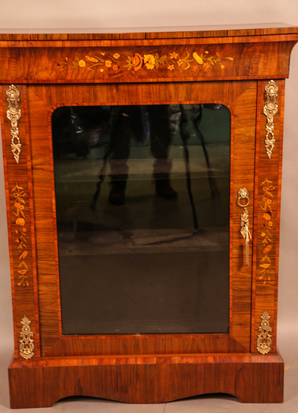 A Victorian figured walnut pier cabinet featuring a single glazed door, floral marquetry inlay, and ornate gilt-metal mounts.