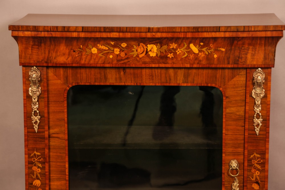 A Victorian figured walnut pier cabinet featuring a single glazed door, floral marquetry inlay, and ornate gilt-metal mounts. View V