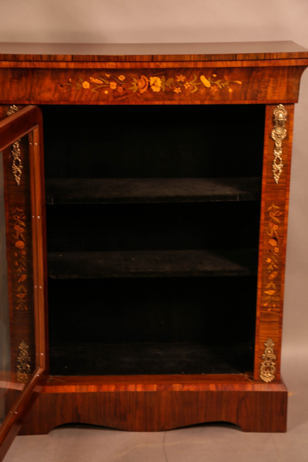 A Victorian figured walnut pier cabinet featuring a single glazed door, floral marquetry inlay, and ornate gilt-metal mounts. View VI