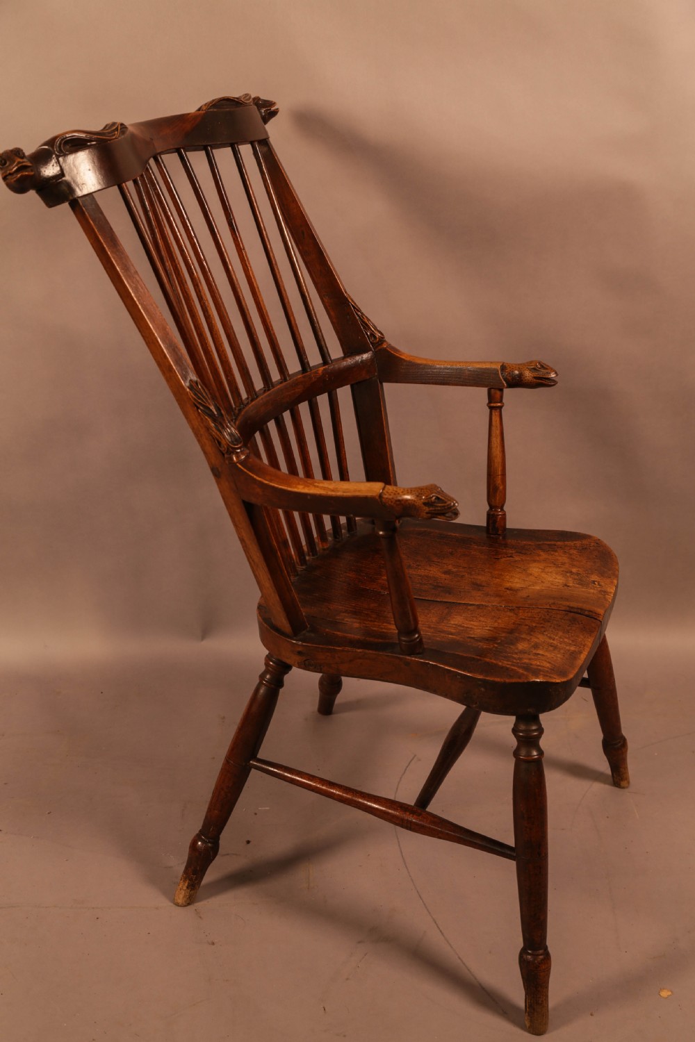 A dark brown antique wooden Windsor armchair featuring vertical spindles, a contoured saddle seat, and hand-carved snake head terminals on the arms and top rail. View II