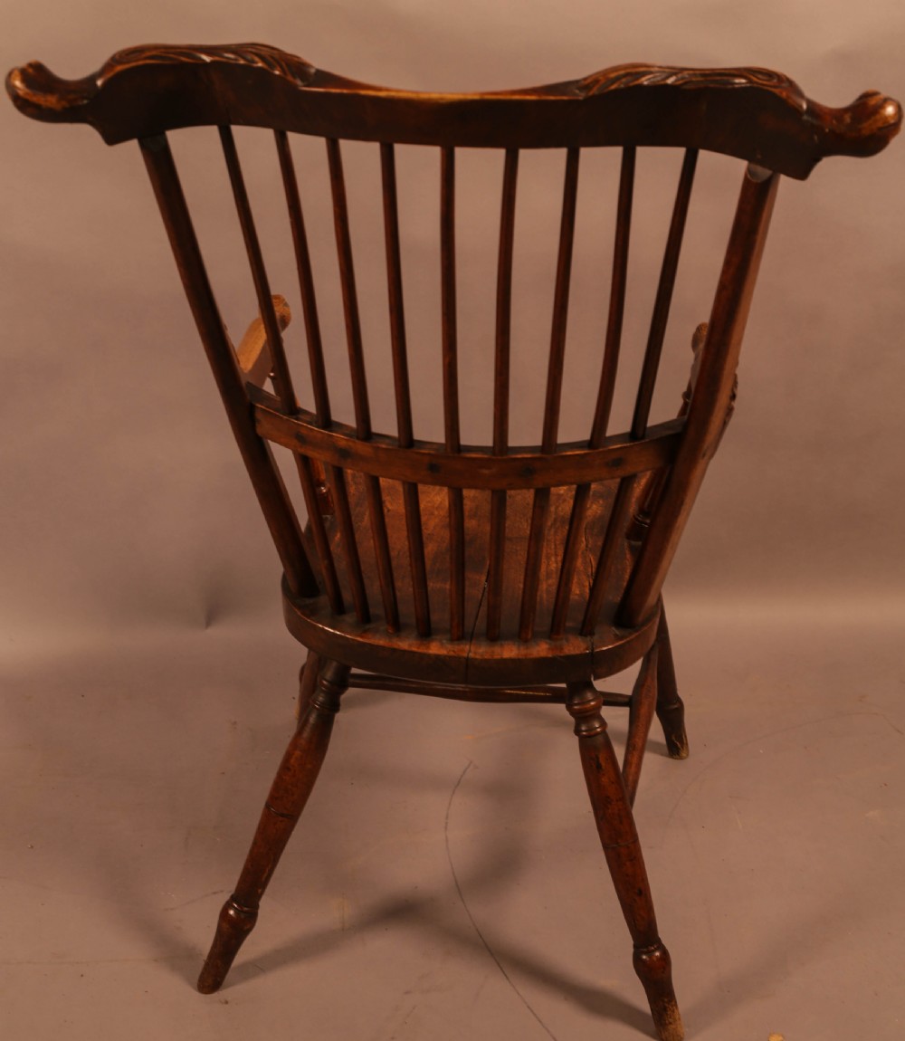 A dark brown antique wooden Windsor armchair featuring vertical spindles, a contoured saddle seat, and hand-carved snake head terminals on the arms and top rail. View III