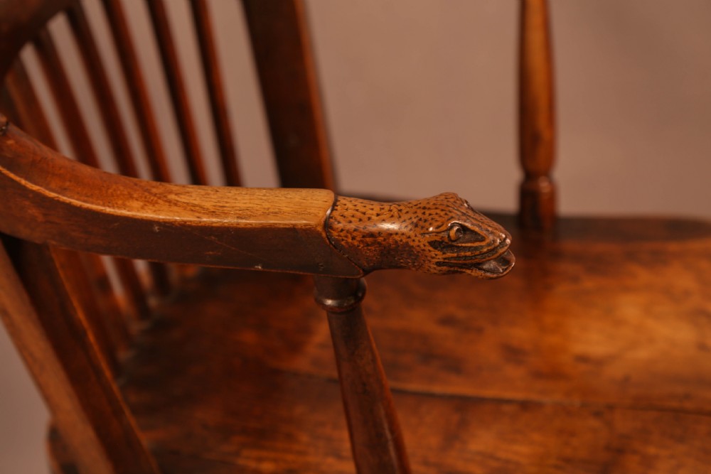 A dark brown antique wooden Windsor armchair featuring vertical spindles, a contoured saddle seat, and hand-carved snake head terminals on the arms and top rail. View IV
