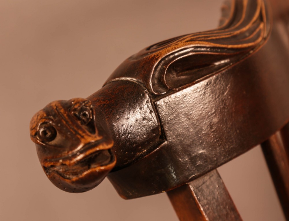 A dark brown antique wooden Windsor armchair featuring vertical spindles, a contoured saddle seat, and hand-carved snake head terminals on the arms and top rail. View VI