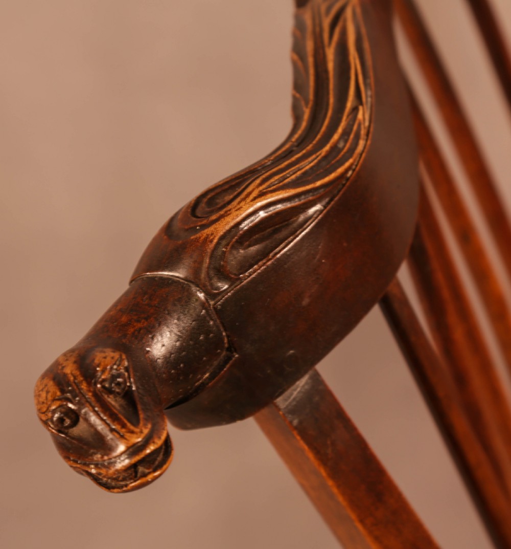 A dark brown antique wooden Windsor armchair featuring vertical spindles, a contoured saddle seat, and hand-carved snake head terminals on the arms and top rail. View VIII