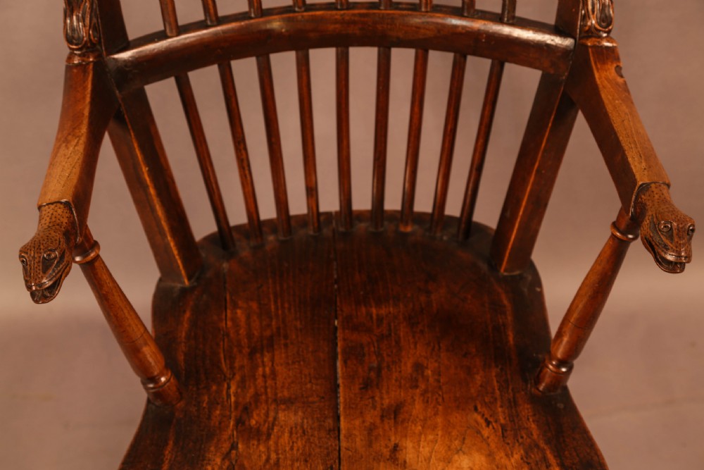 A dark brown antique wooden Windsor armchair featuring vertical spindles, a contoured saddle seat, and hand-carved snake head terminals on the arms and top rail. View XI