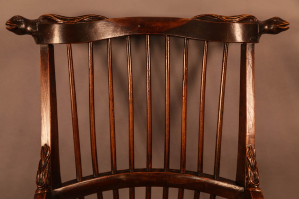 A dark brown antique wooden Windsor armchair featuring vertical spindles, a contoured saddle seat, and hand-carved snake head terminals on the arms and top rail. View XII