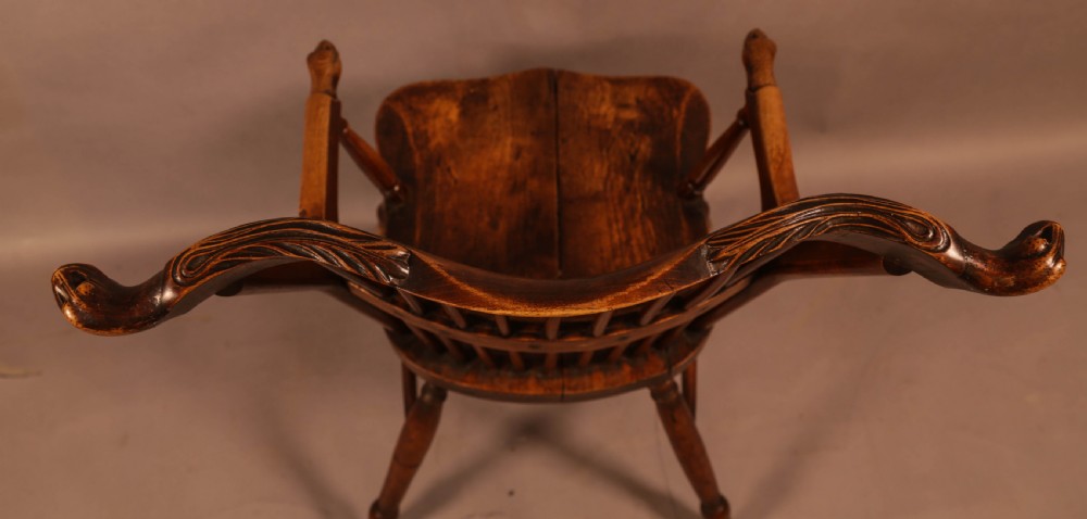 A dark brown antique wooden Windsor armchair featuring vertical spindles, a contoured saddle seat, and hand-carved snake head terminals on the arms and top rail. View XIII