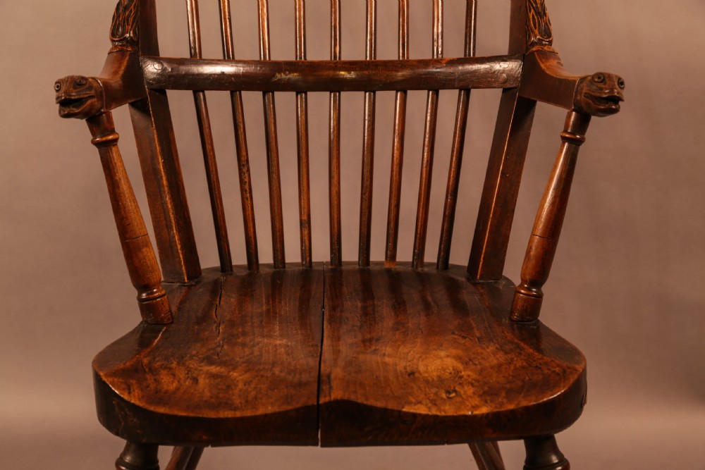 A dark brown antique wooden Windsor armchair featuring vertical spindles, a contoured saddle seat, and hand-carved snake head terminals on the arms and top rail. View XVIII