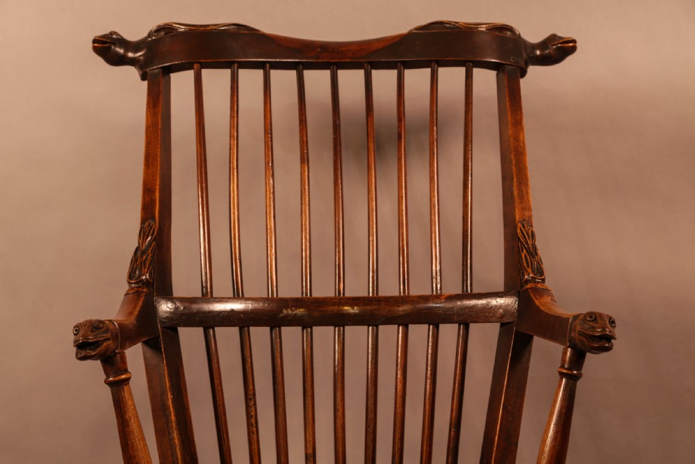 A dark brown antique wooden Windsor armchair featuring vertical spindles, a contoured saddle seat, and hand-carved snake head terminals on the arms and top rail. View XIX