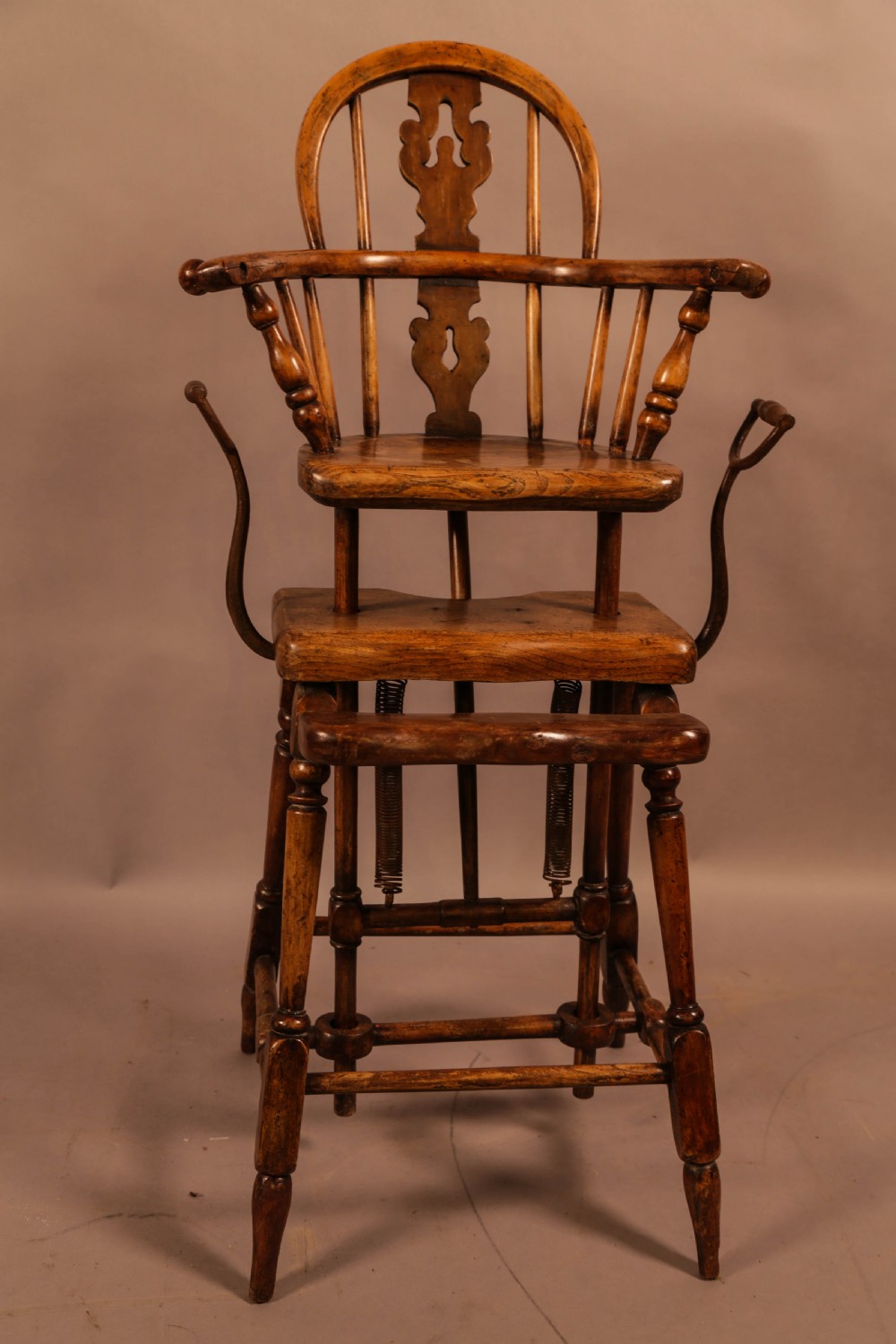 An antique Victorian yew wood child exercise chair featuring a hoop-back top seat, side metal handles, coiled steel springs, and turned legs.