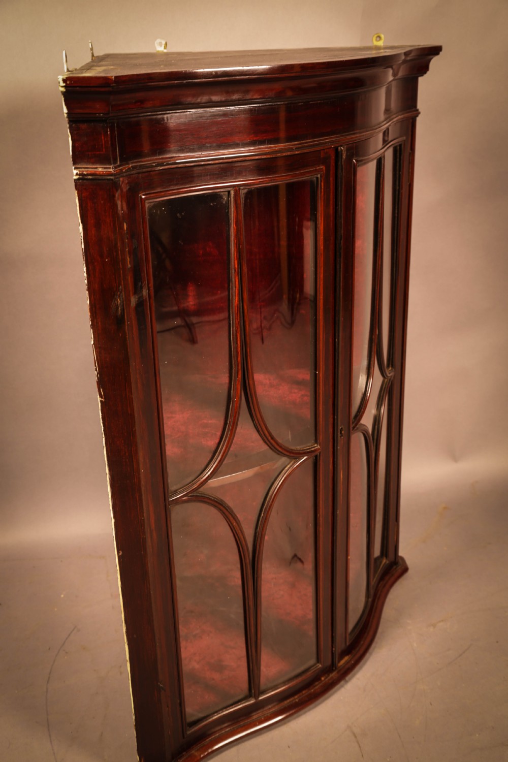 A dark mahogany wall-hanging corner cupboard featuring glazed double doors with serpentine curved fronts and decorative astragal glazing bars. View IV