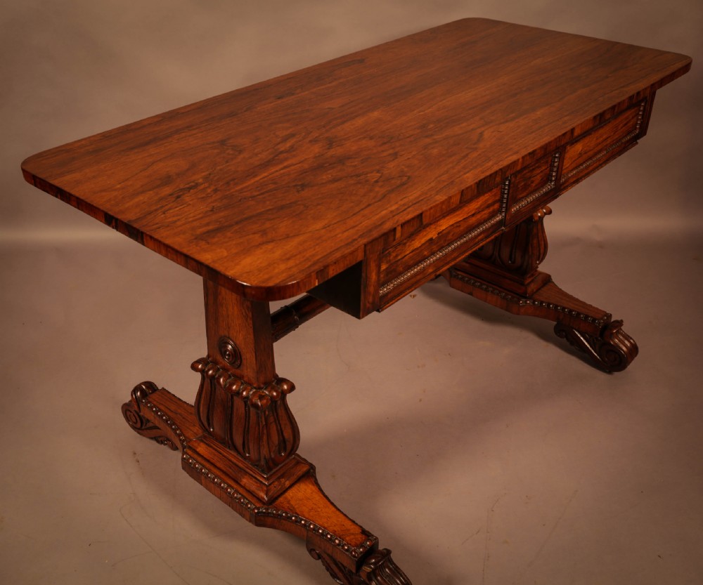 A William IV rosewood library table featuring a rectangular top with rounded corners, frieze drawers, a turned central stretcher, and carved pedestal legs. View II
