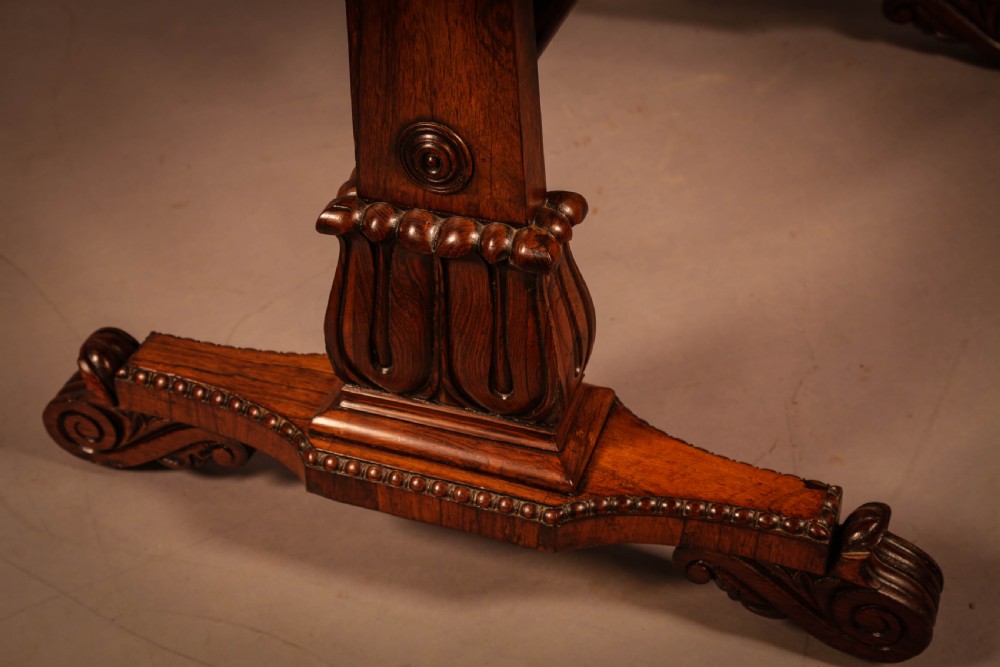 A William IV rosewood library table featuring a rectangular top with rounded corners, frieze drawers, a turned central stretcher, and carved pedestal legs. View IV