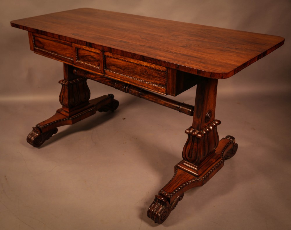 A William IV rosewood library table featuring a rectangular top with rounded corners, frieze drawers, a turned central stretcher, and carved pedestal legs. View VI