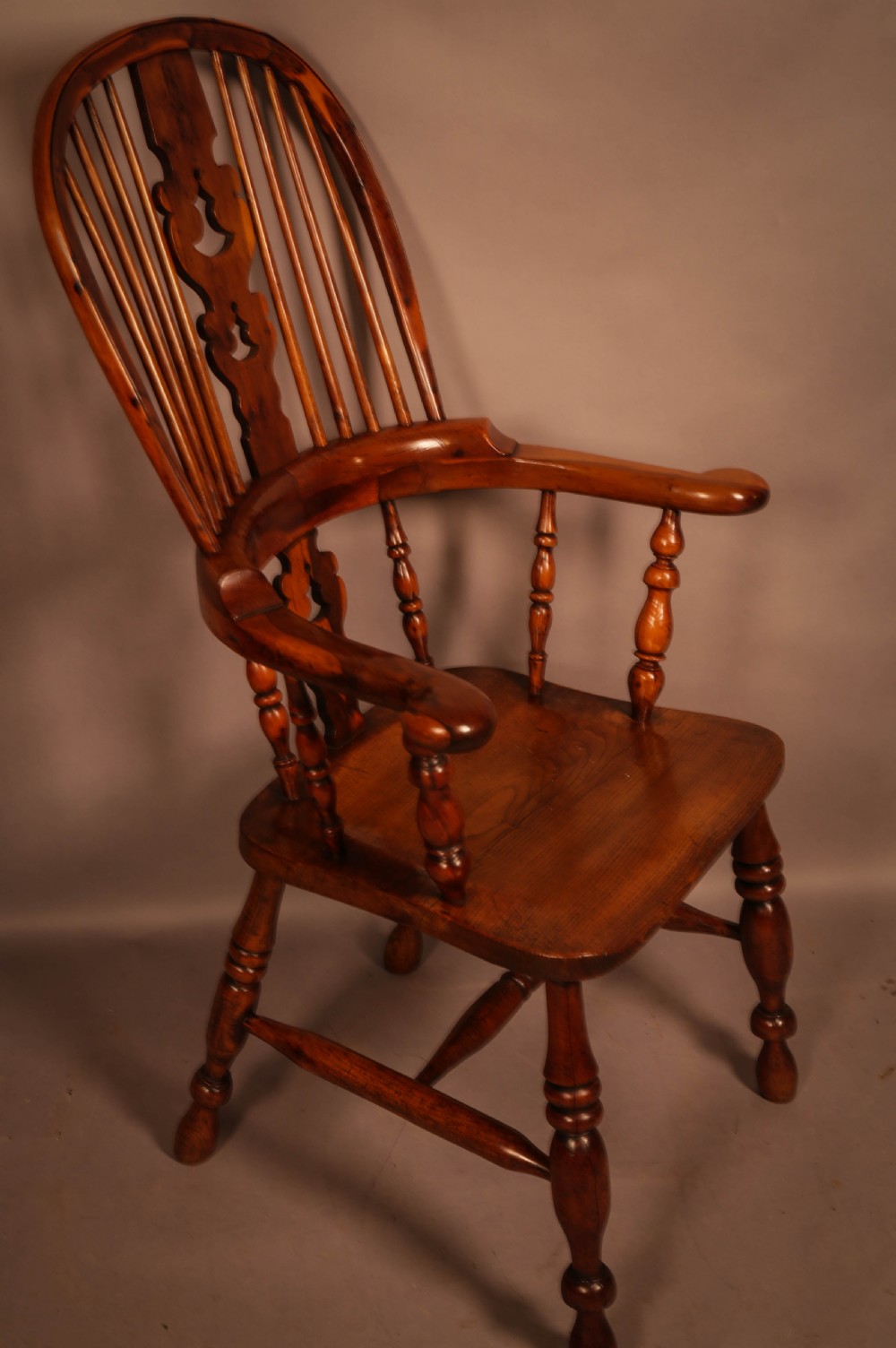 A high-back yew wood Windsor armchair featuring a pierced back splat, spindle backrest, broad armrests, turned legs, and stretchers.