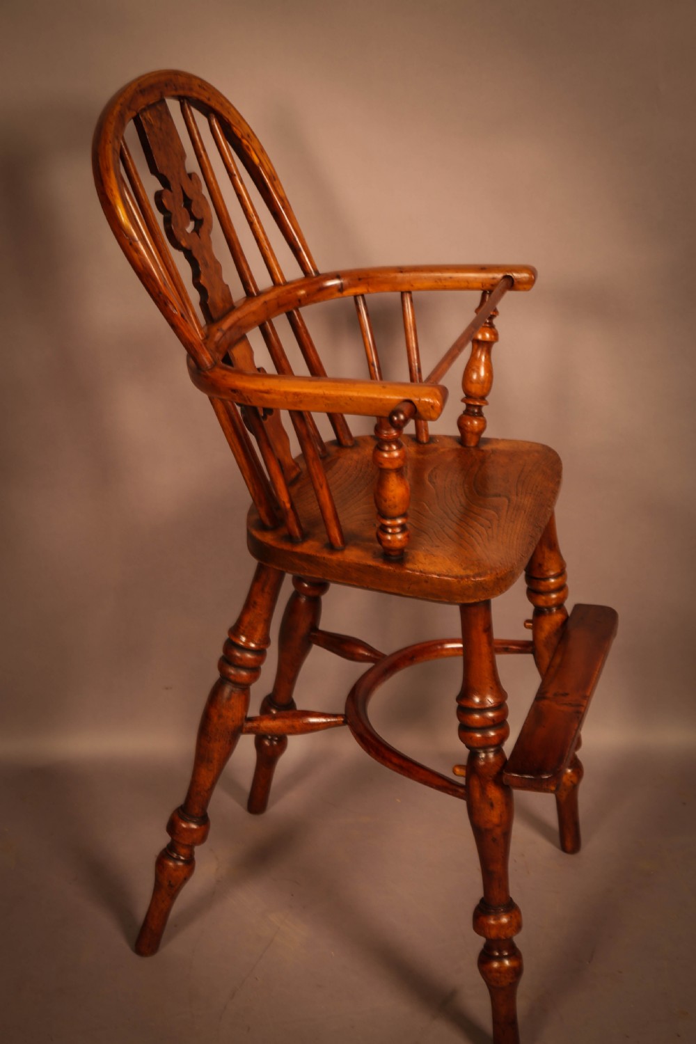 A yew wood Windsor childs high chair with a pierced splat back, turned legs, footrest, and safety bar. View II