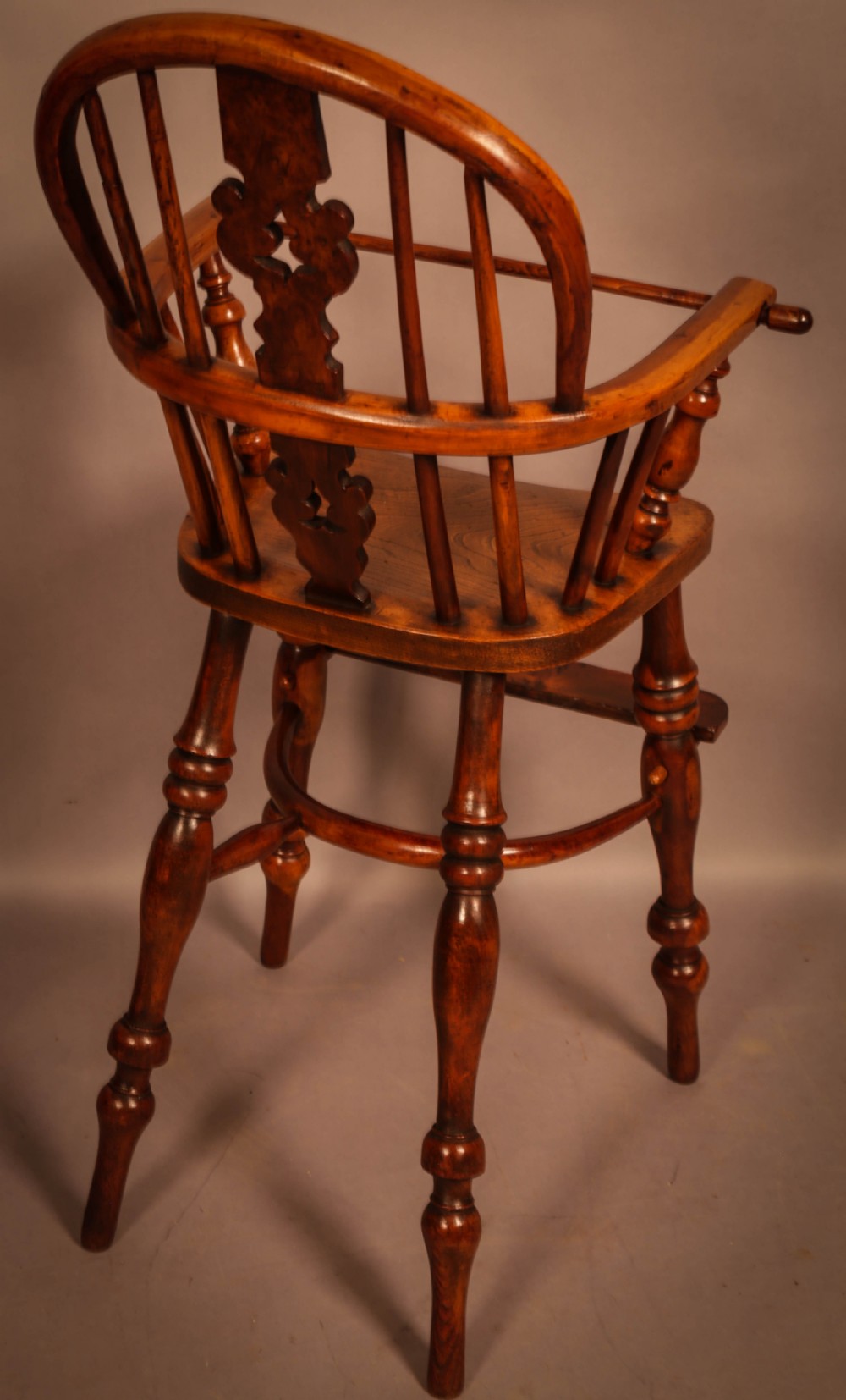 A yew wood Windsor childs high chair with a pierced splat back, turned legs, footrest, and safety bar. View III