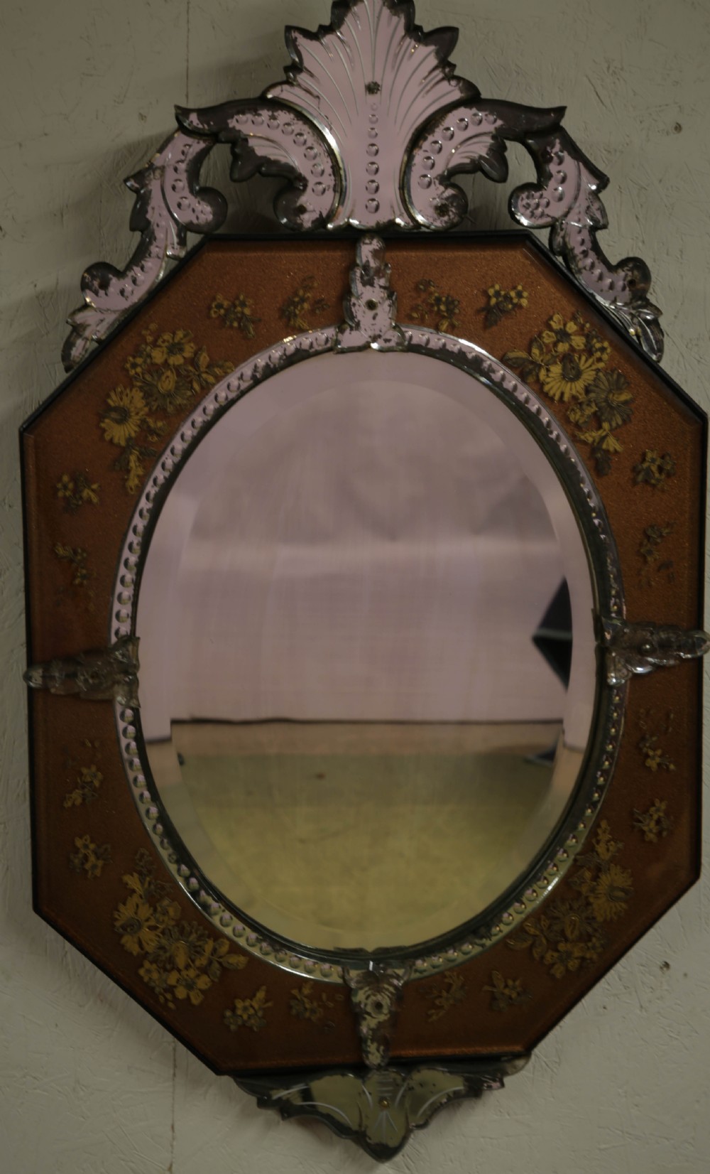 An octagonal Venetian wall mirror with a central oval plate, amber etched glass borders, and a decorative glass top crest.