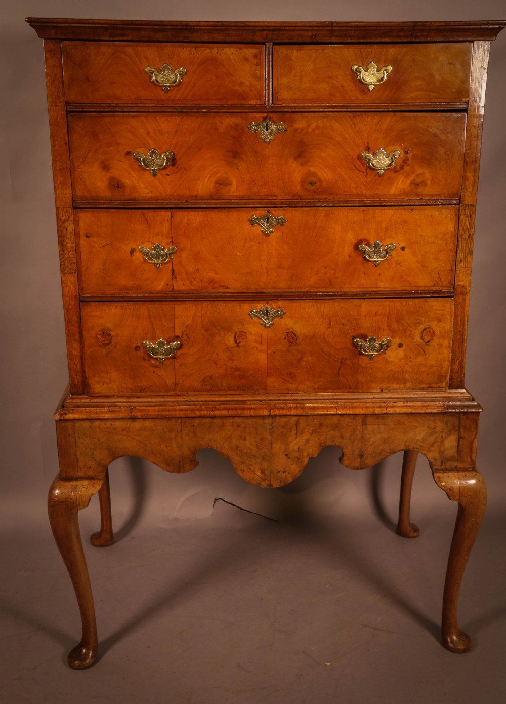 An 18th-century English walnut chest on stand featuring figured veneers, brass engraved escutcheons, a shaped apron frieze, and cabriole legs with pad feet.