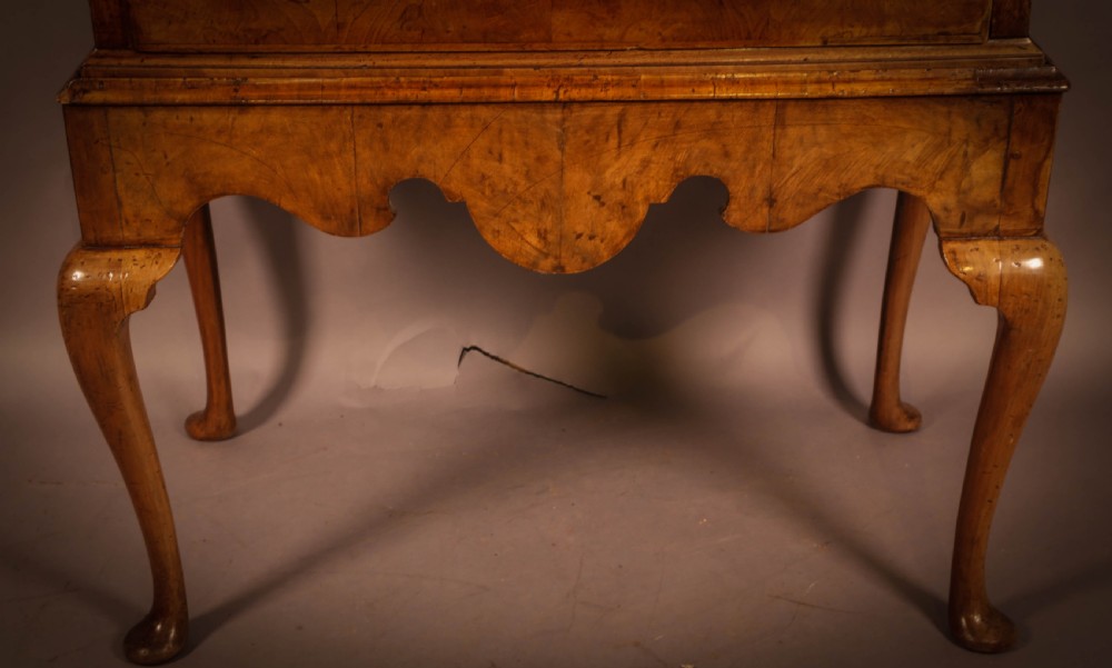 An 18th-century English walnut chest on stand featuring figured veneers, brass engraved escutcheons, a shaped apron frieze, and cabriole legs with pad feet. View VI