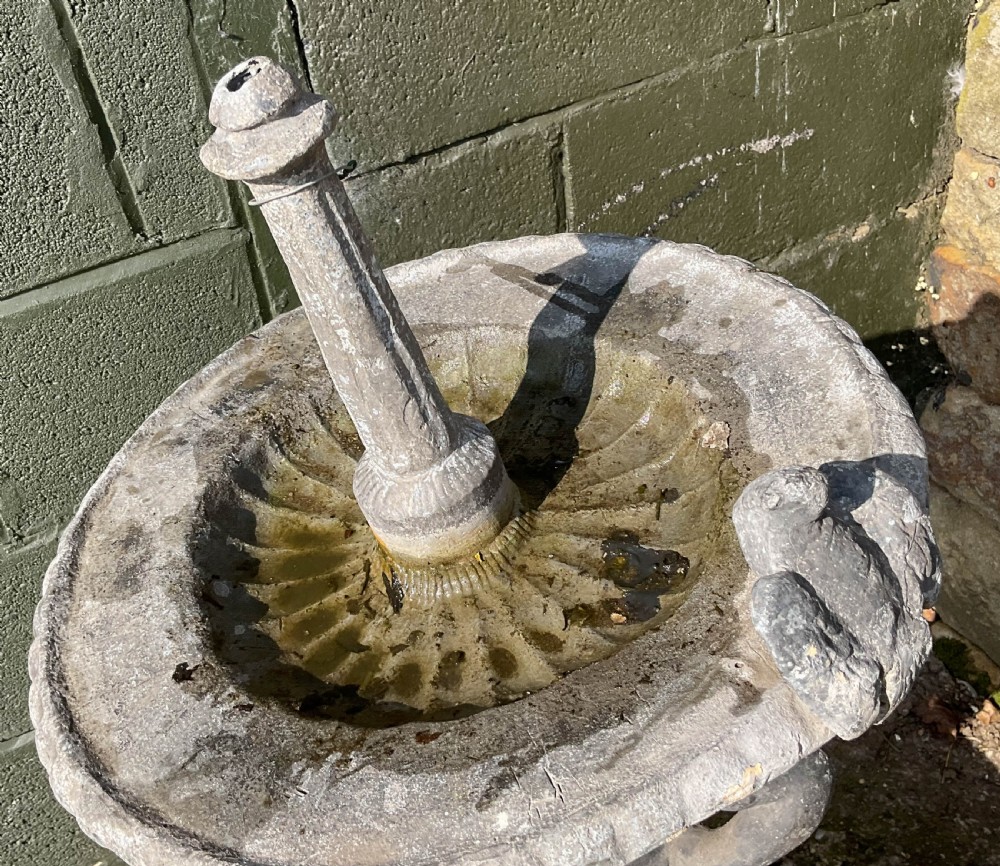 A cast lead fountain featuring a figural base supporting a shallow basin and central spout, mounted upon a rough-hewn stone plinth. View IV