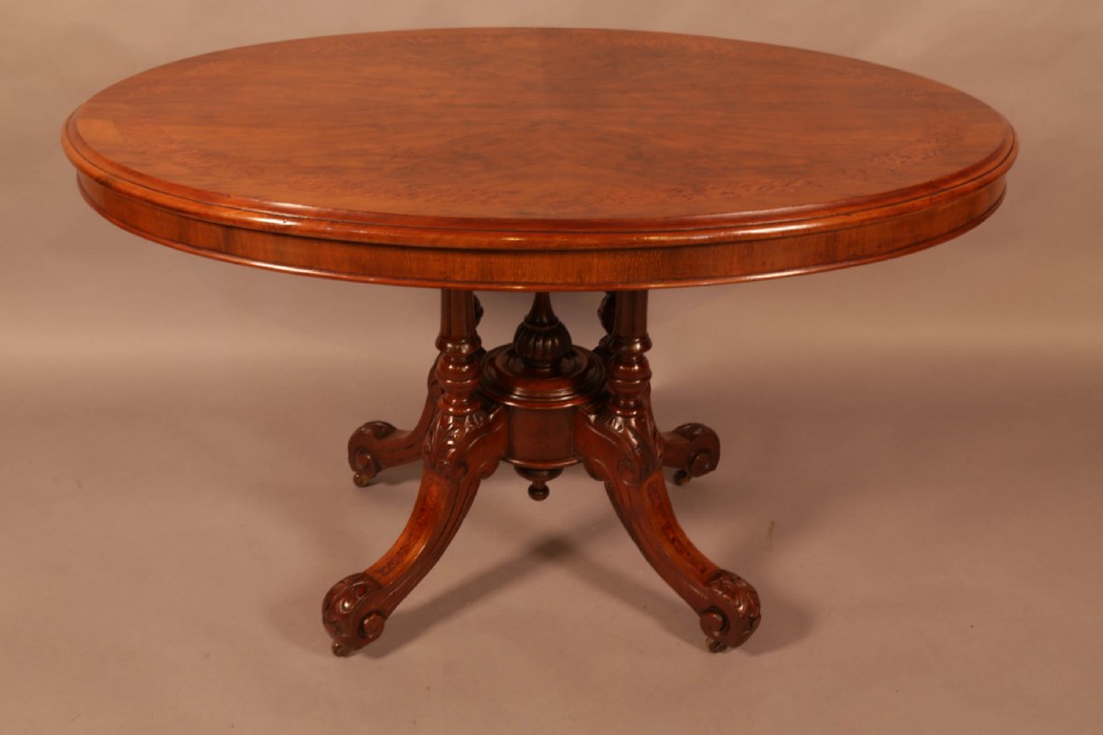 An oval Victorian burr walnut table featuring a figured veneer top and a central carved pedestal with four scroll feet. View II