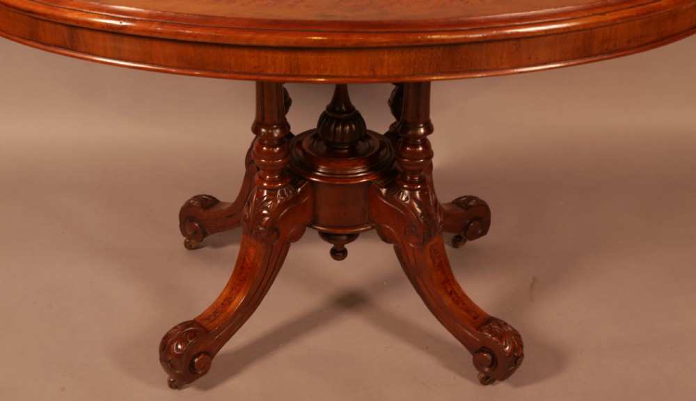 An oval Victorian burr walnut table featuring a figured veneer top and a central carved pedestal with four scroll feet. View III
