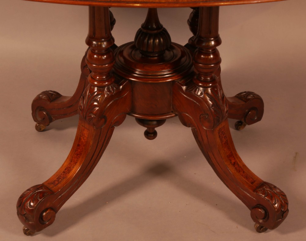 An oval Victorian burr walnut table featuring a figured veneer top and a central carved pedestal with four scroll feet. View IV