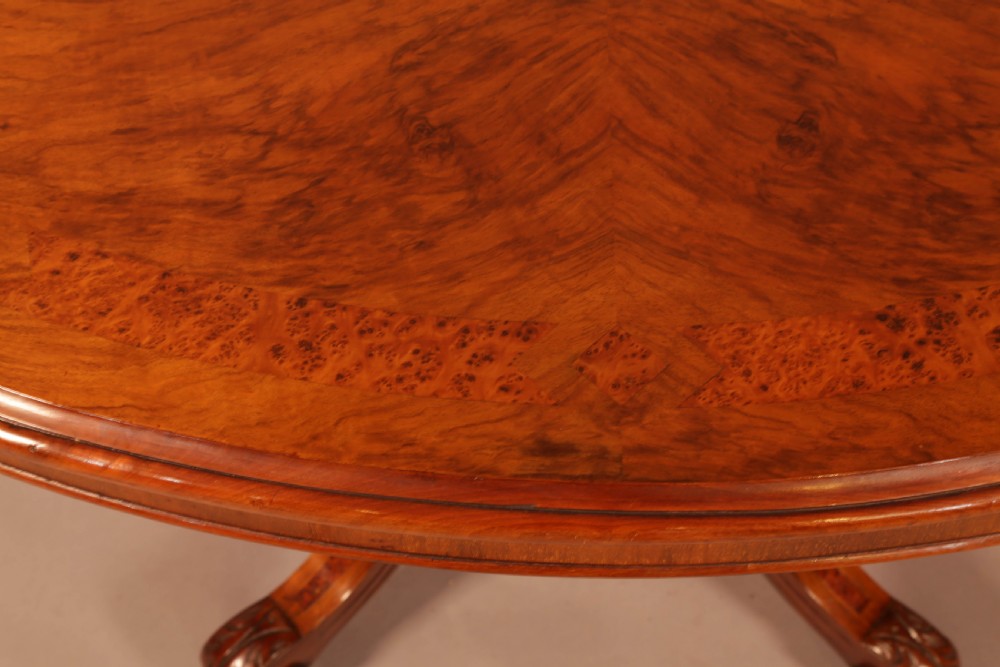 An oval Victorian burr walnut table featuring a figured veneer top and a central carved pedestal with four scroll feet. View VI
