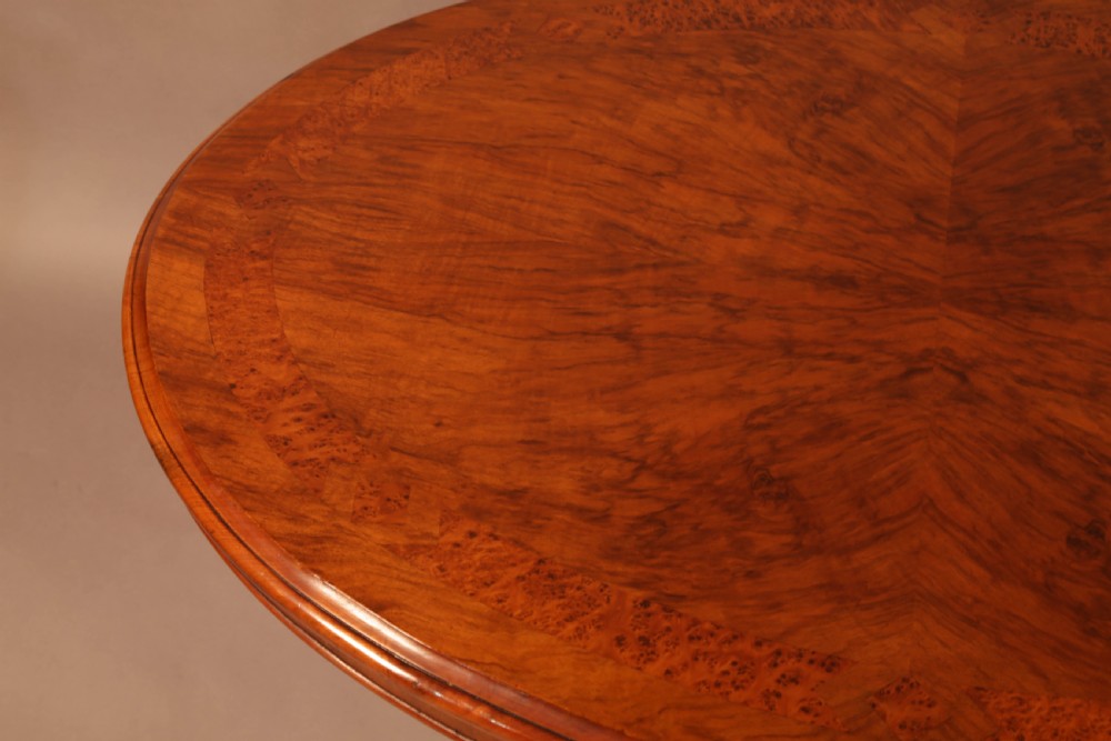 An oval Victorian burr walnut table featuring a figured veneer top and a central carved pedestal with four scroll feet. View VII