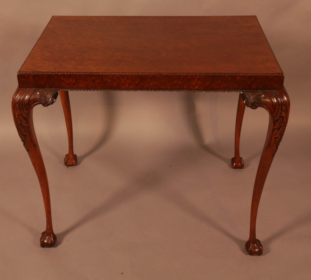 A Chippendale style wooden silver table featuring cabriole legs with carved knees, ball and claw feet, and a rectangular burr-veneered top.