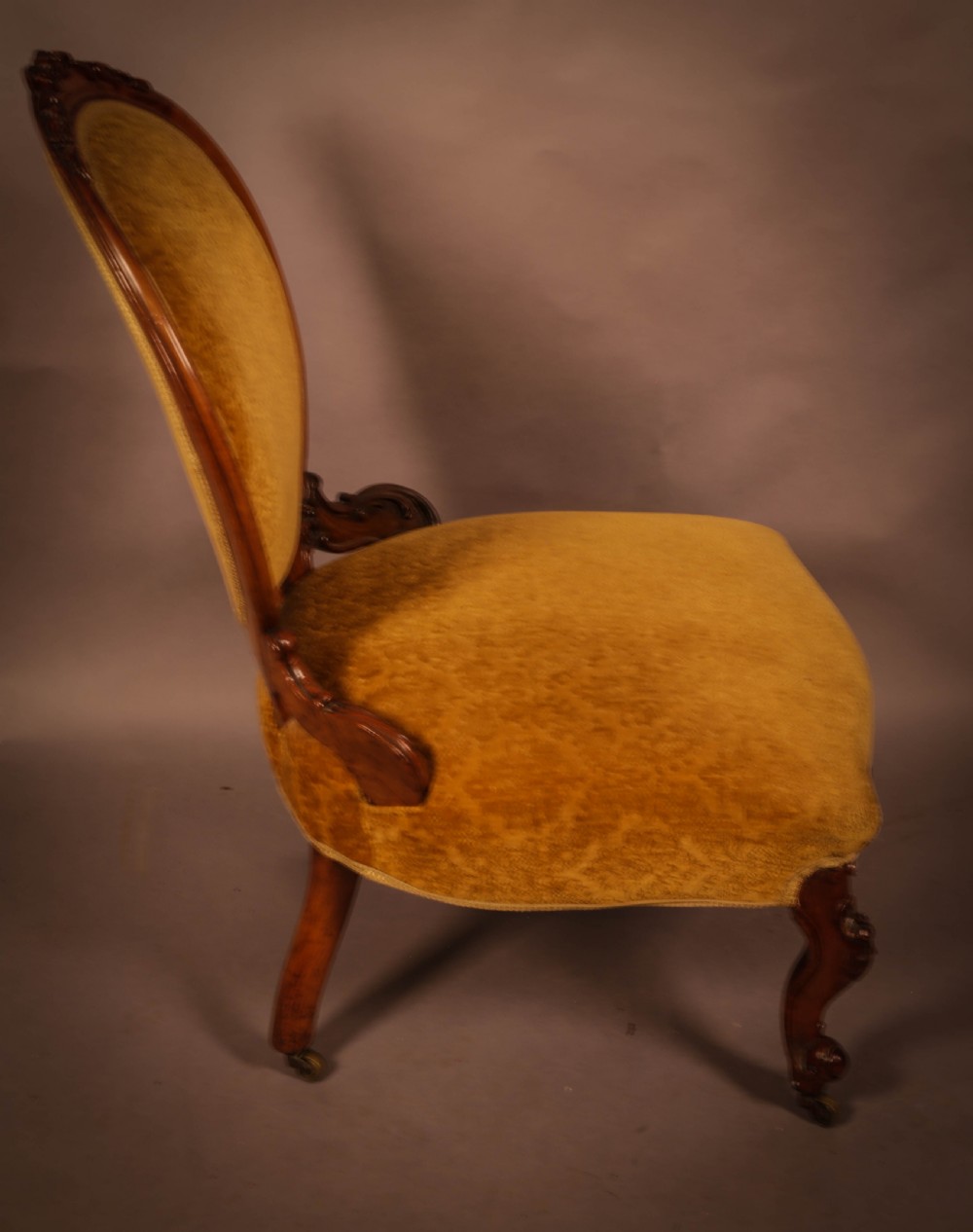 A Victorian walnut nursing chair featuring carved framework, an oval backrest, and golden patterned upholstery. View III