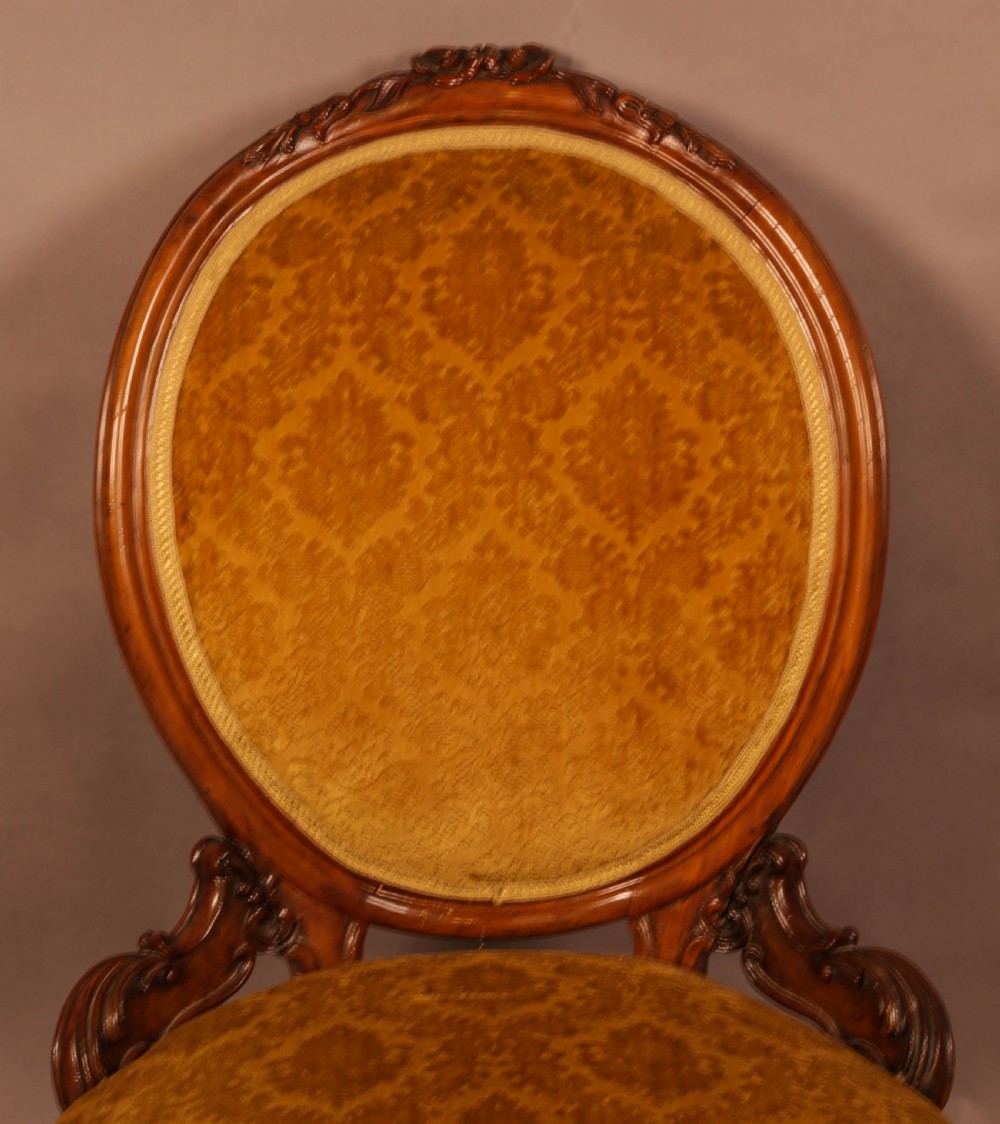 A Victorian walnut nursing chair featuring carved framework, an oval backrest, and golden patterned upholstery. View V