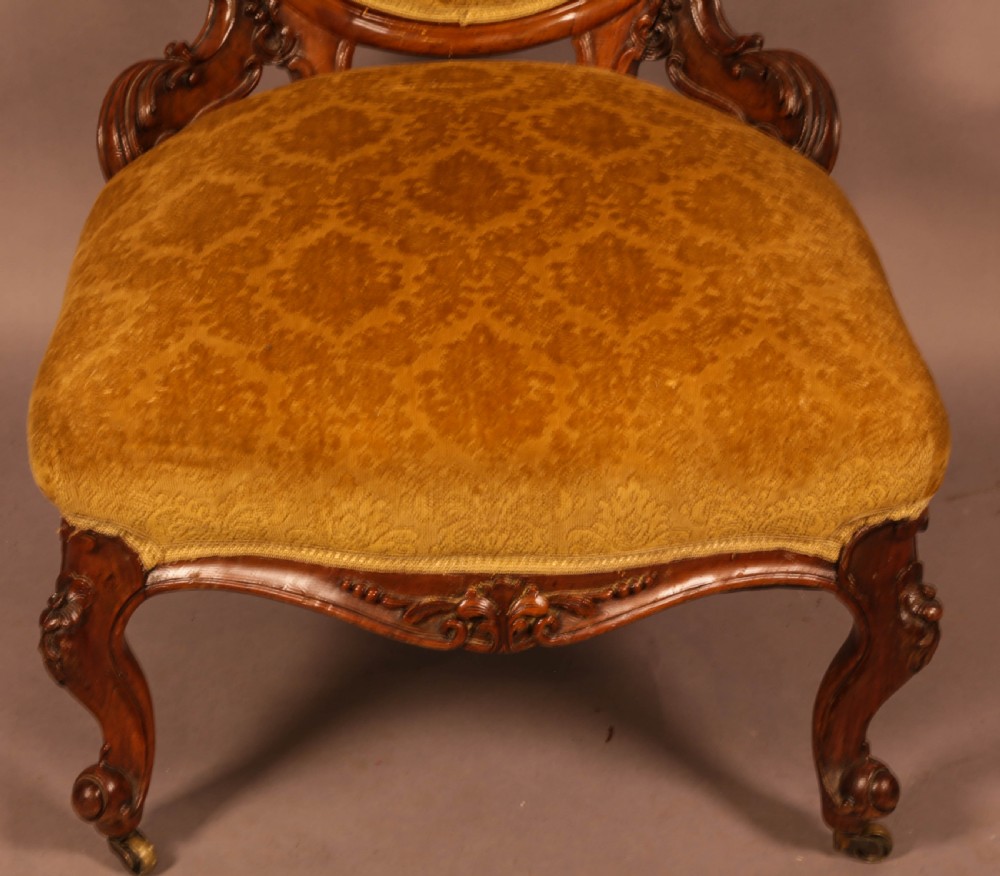 A Victorian walnut nursing chair featuring carved framework, an oval backrest, and golden patterned upholstery. View VI