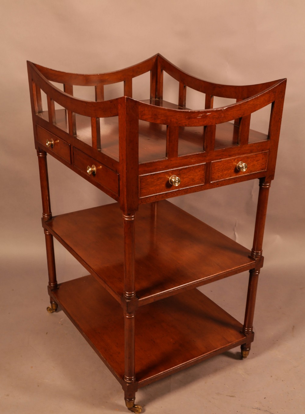 A three-tier mahogany library book stand featuring open shelves, two small drawers with brass knobs, and turned supports on castors. View III