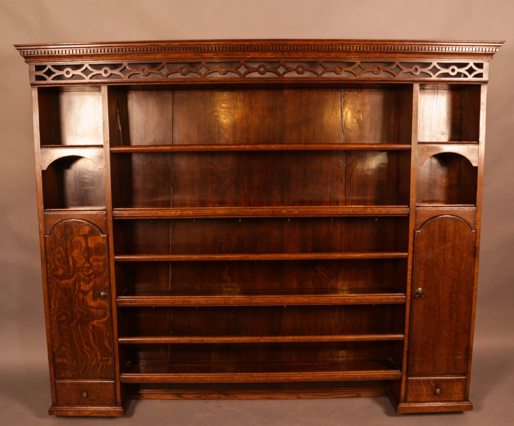 Large dark oak plate rack featuring open shelves with grooved runners, flanked by two side cupboards, topped with a geometric pierced fretwork frieze and dentil cornice.