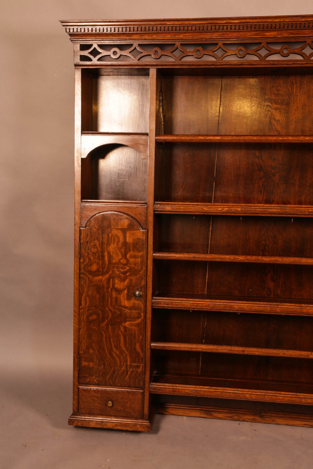 Large dark oak plate rack featuring open shelves with grooved runners, flanked by two side cupboards, topped with a geometric pierced fretwork frieze and dentil cornice. View II