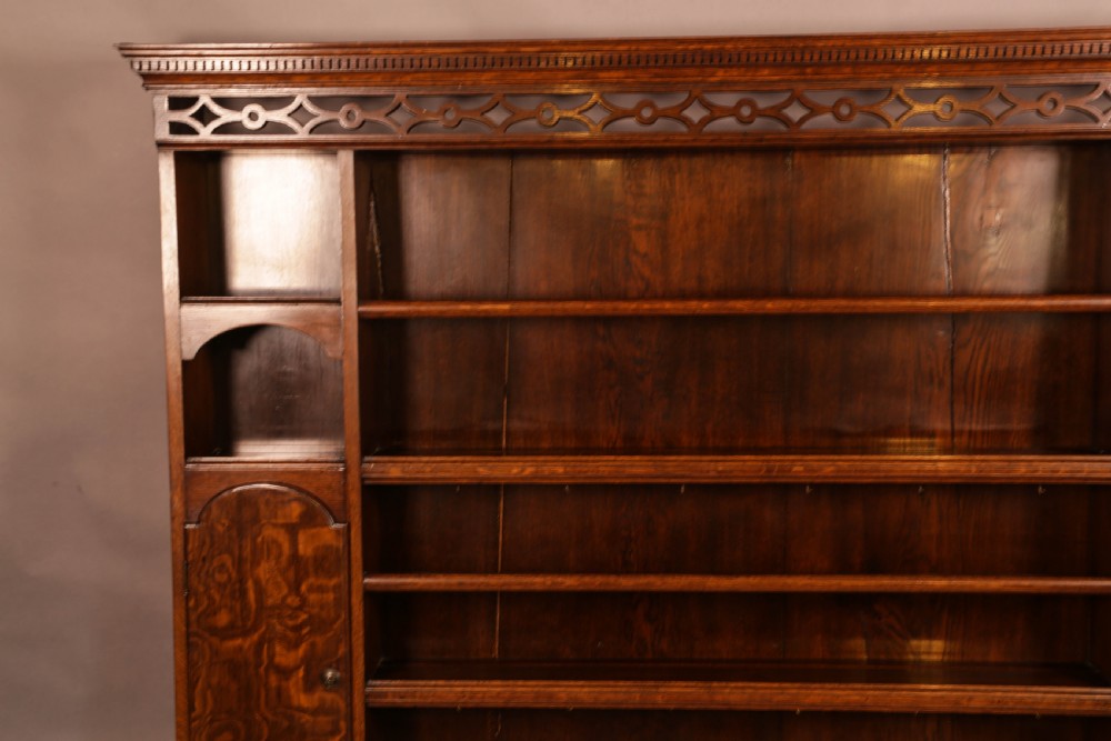 Large dark oak plate rack featuring open shelves with grooved runners, flanked by two side cupboards, topped with a geometric pierced fretwork frieze and dentil cornice. View III