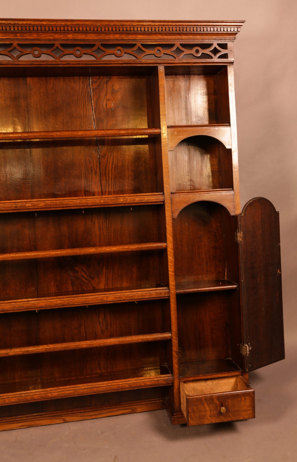 Large dark oak plate rack featuring open shelves with grooved runners, flanked by two side cupboards, topped with a geometric pierced fretwork frieze and dentil cornice. View IV