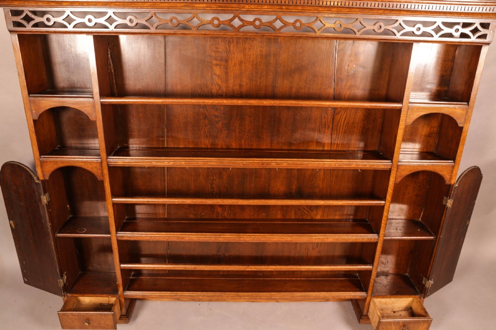 Large dark oak plate rack featuring open shelves with grooved runners, flanked by two side cupboards, topped with a geometric pierced fretwork frieze and dentil cornice. View VI