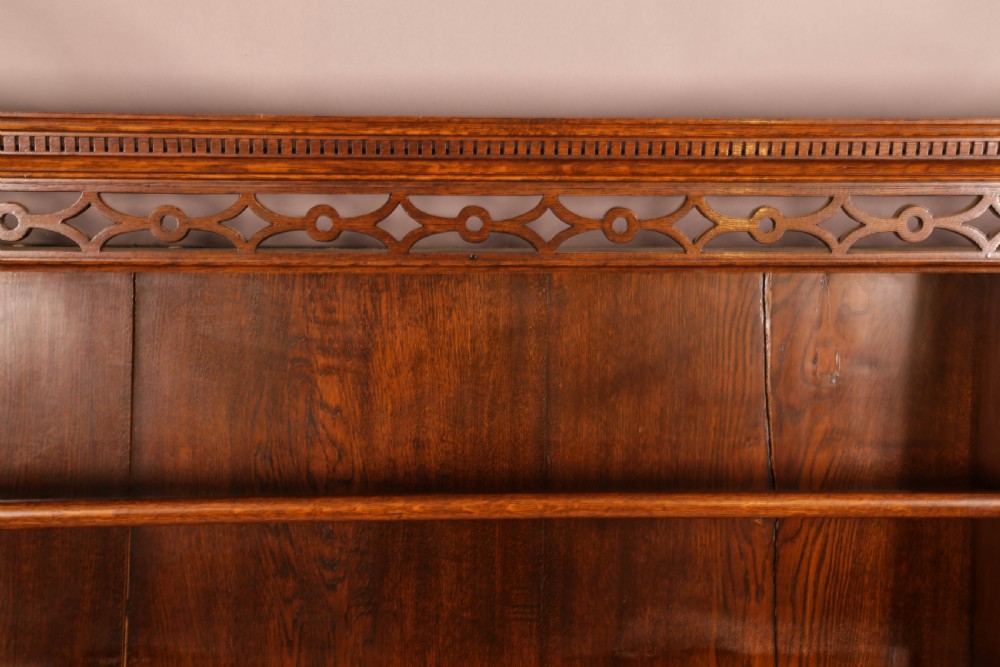 Large dark oak plate rack featuring open shelves with grooved runners, flanked by two side cupboards, topped with a geometric pierced fretwork frieze and dentil cornice. View VII
