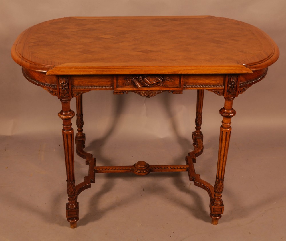 An antique French walnut window table featuring a geometric parquetry top, carved aprons, turned fluted legs, and a shaped cross-stretcher.