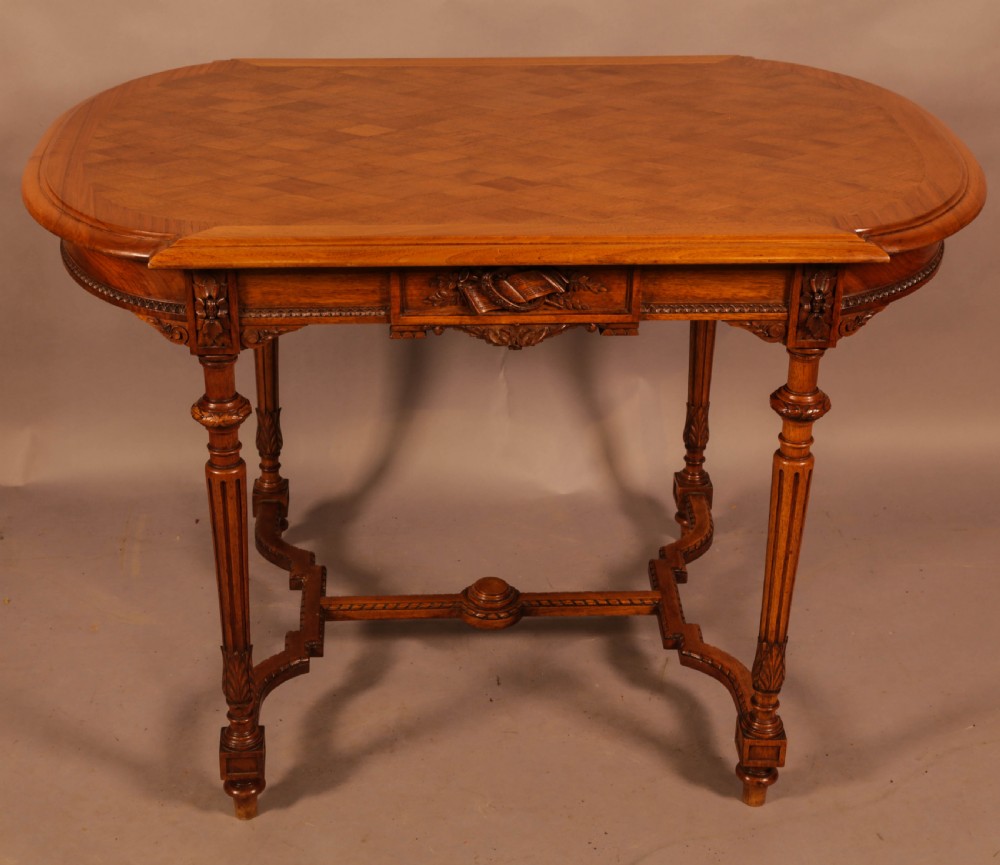 An antique French walnut window table featuring a geometric parquetry top, carved aprons, turned fluted legs, and a shaped cross-stretcher. View II