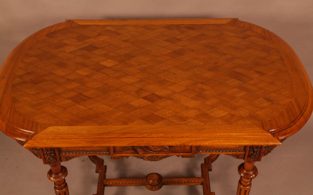 An antique French walnut window table featuring a geometric parquetry top, carved aprons, turned fluted legs, and a shaped cross-stretcher. View III