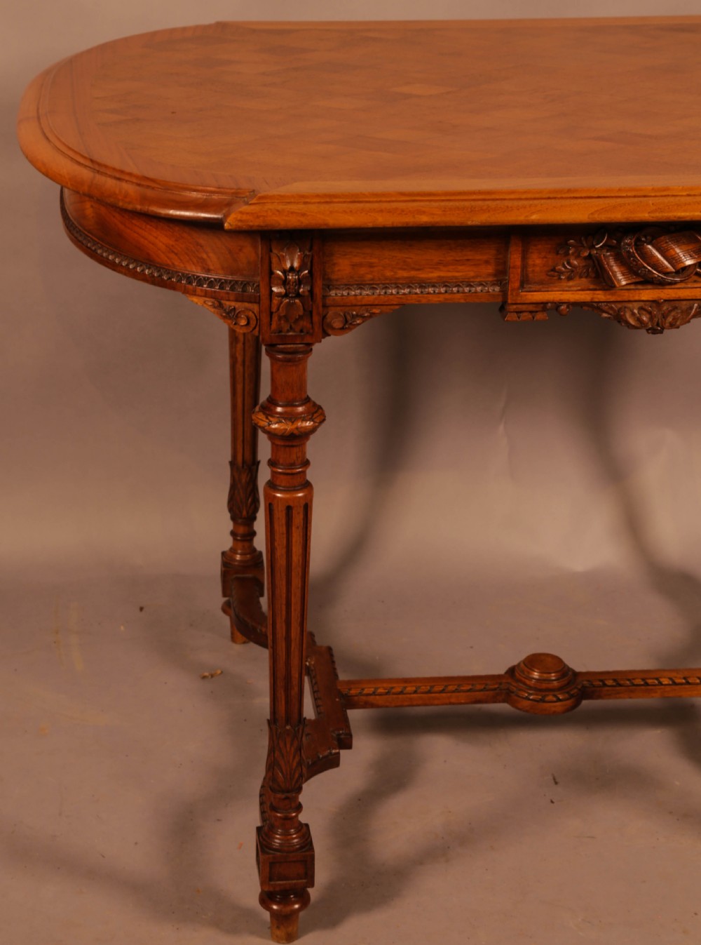An antique French walnut window table featuring a geometric parquetry top, carved aprons, turned fluted legs, and a shaped cross-stretcher. View IV