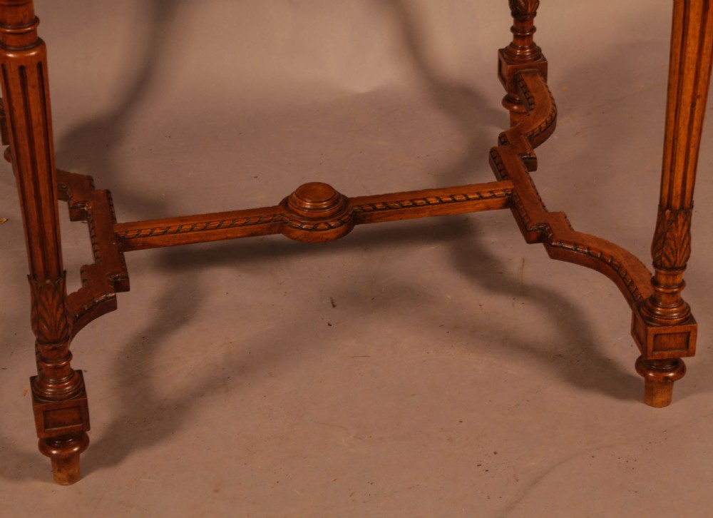 An antique French walnut window table featuring a geometric parquetry top, carved aprons, turned fluted legs, and a shaped cross-stretcher. View V